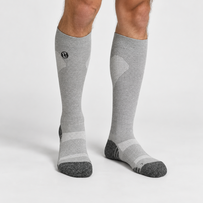 Male model wearing heather grey compression sock with black toe and heel on light grey background