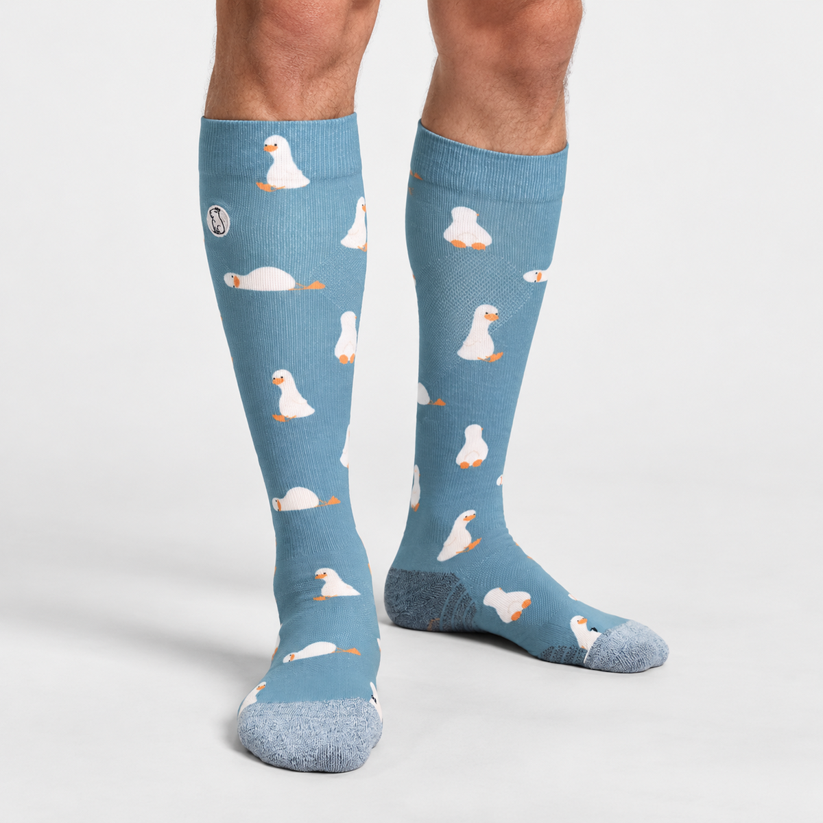 Male model wearing blue/teal compression sock with print featuring various ducks on light grey background