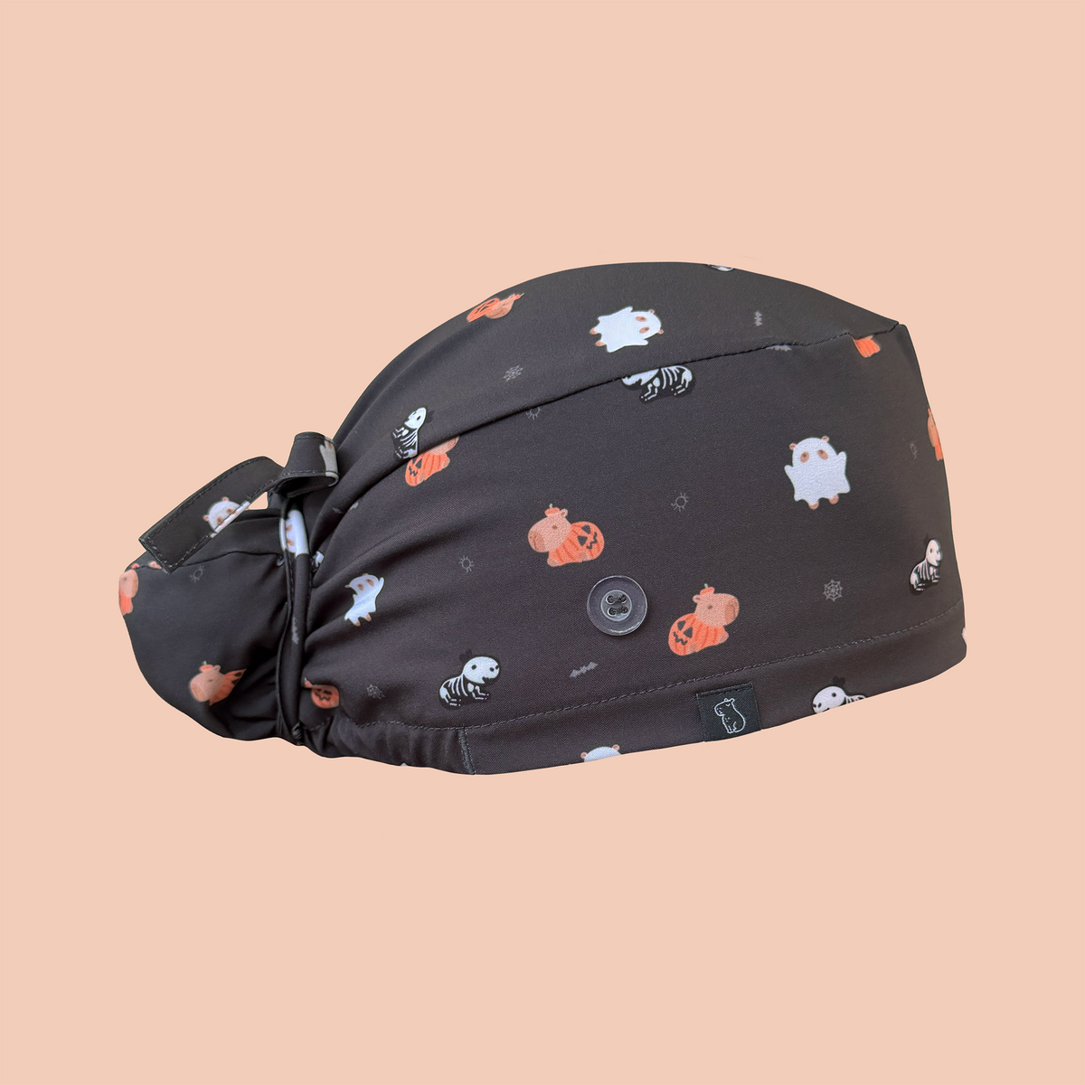Side view of black bun scrub cap featuring capybaras wearing pumpkin, ghost, and skeleton costumes