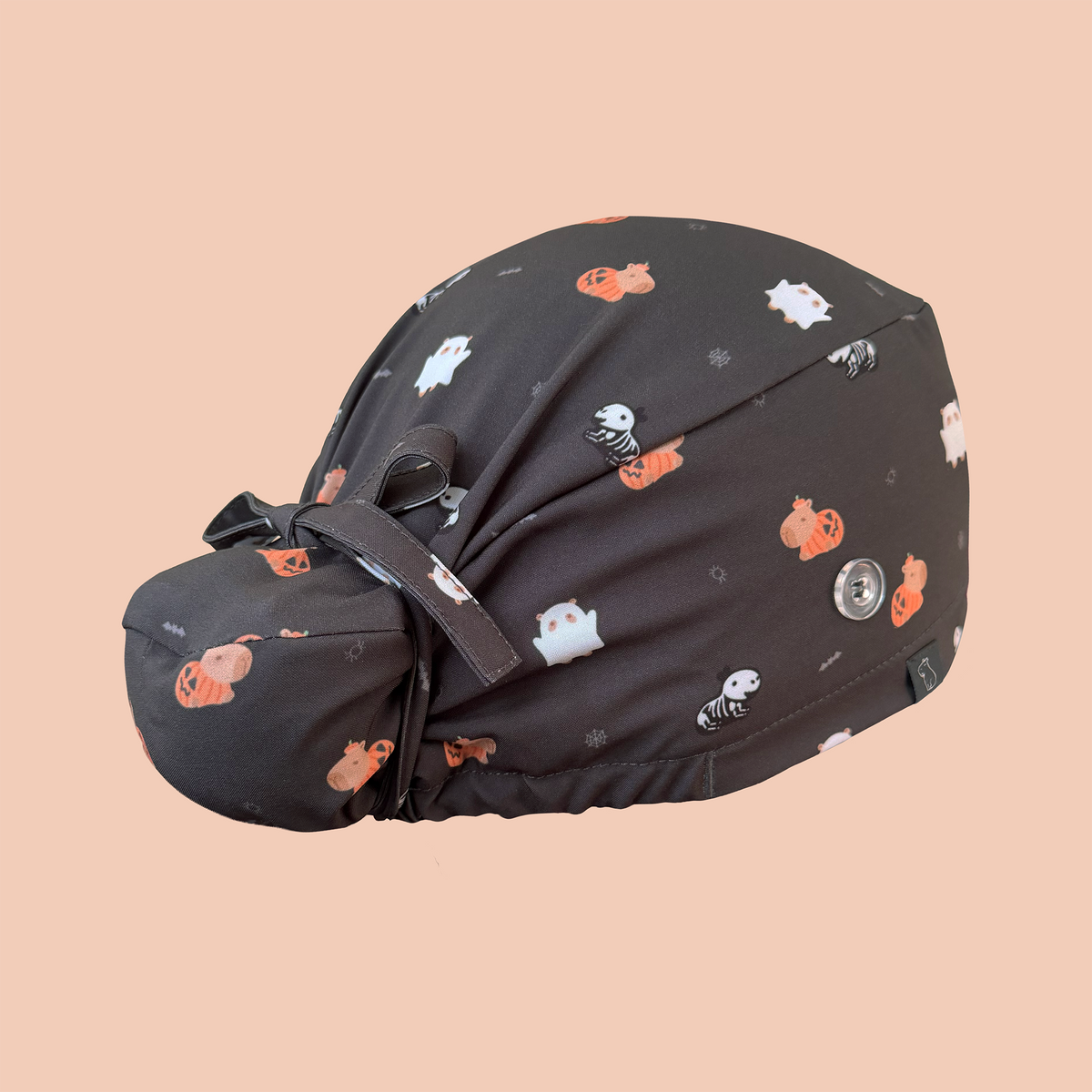 Rear view of black bun scrub cap featuring capybaras wearing pumpkin, ghost, and skeleton costumes