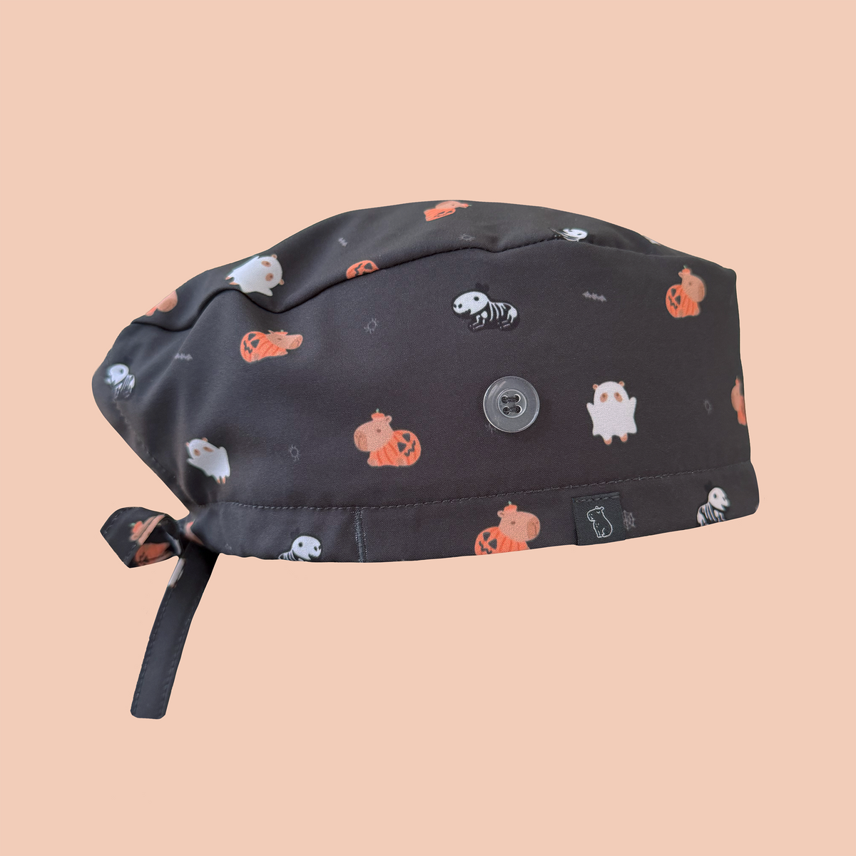 Side view of black classic scrub cap featuring capybaras wearing pumpkin, ghost, and skeleton costumes