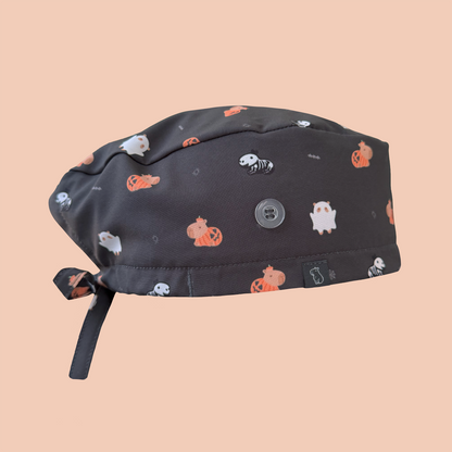 Side view of black classic scrub cap featuring capybaras wearing pumpkin, ghost, and skeleton costumes
