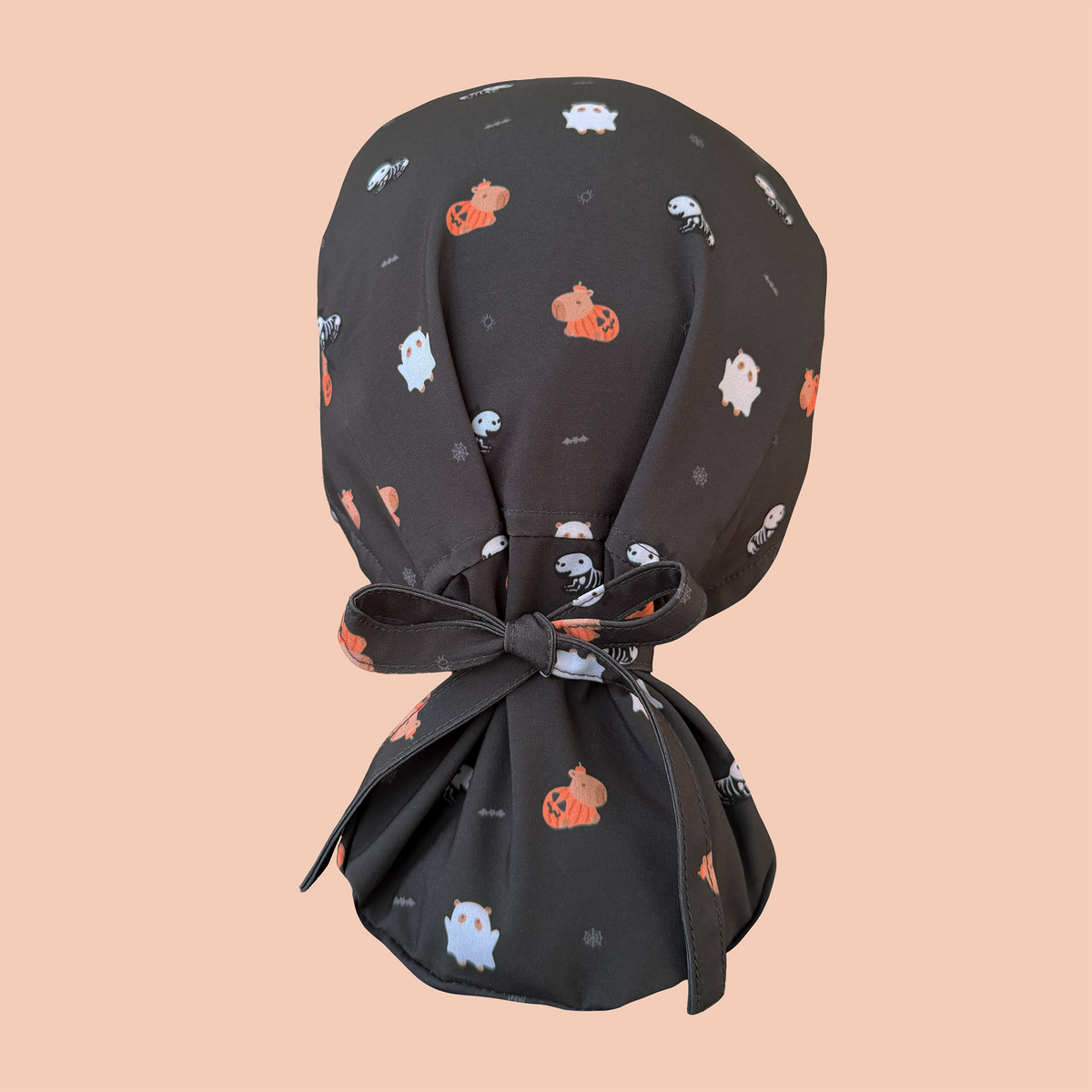 Rear view of black ponytail scrub cap featuring capybaras wearing pumpkin, ghost, and skeleton costumes