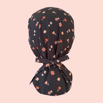 Rear view of ponytail scrub cap featuring pink/peach flowers on a charcoal background
