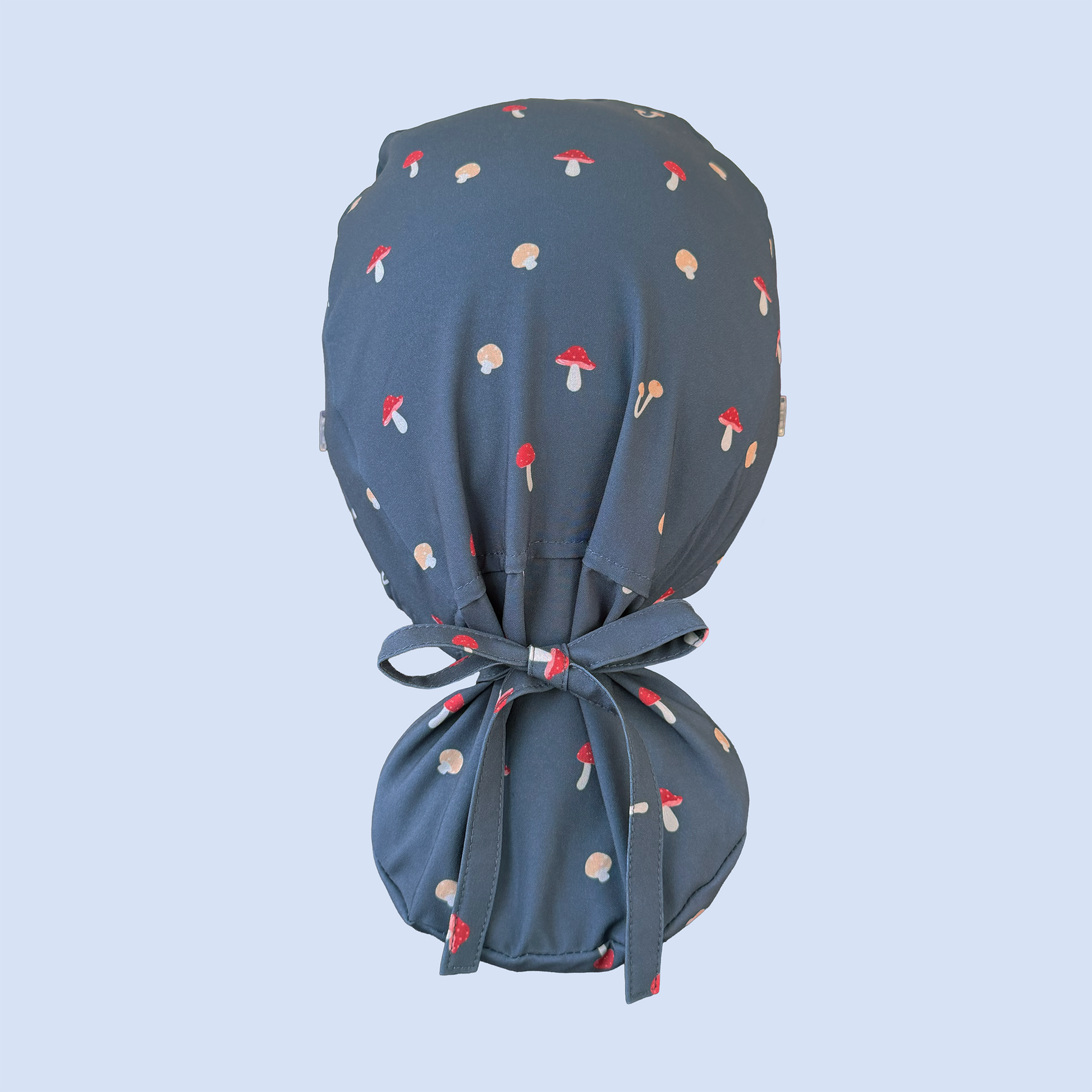 Rear view of blue ponytail scrub cap decorated with a whimsical mushroom print in red, yellow, and white