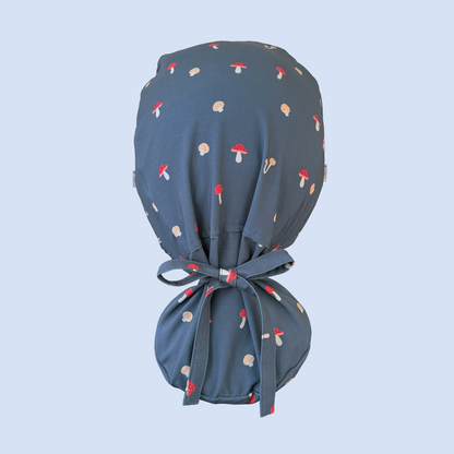 Rear view of blue ponytail scrub cap decorated with a whimsical mushroom print in red, yellow, and white