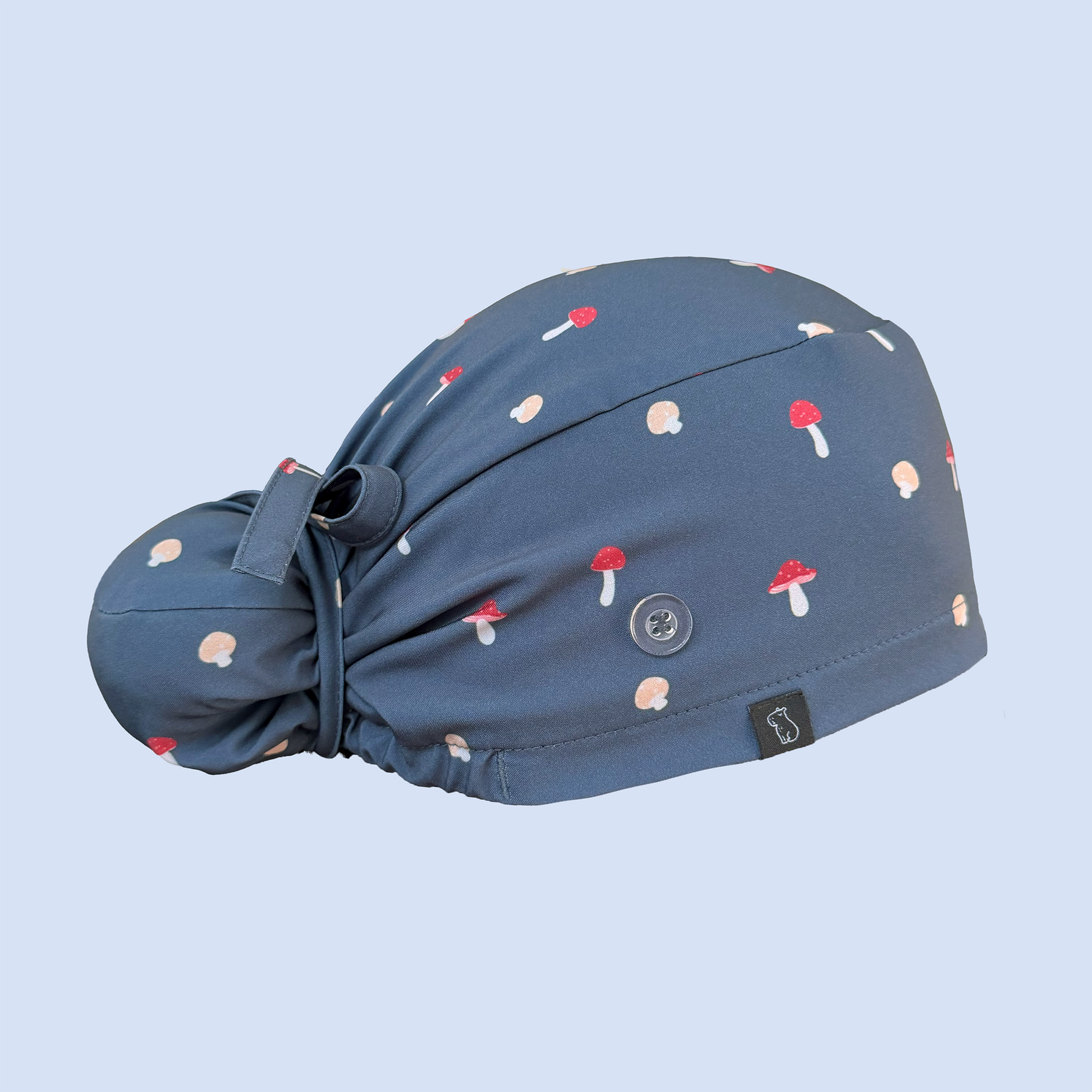 Side view of blue Bun scrub cap decorated with a whimsical mushroom print in red, yellow, and white