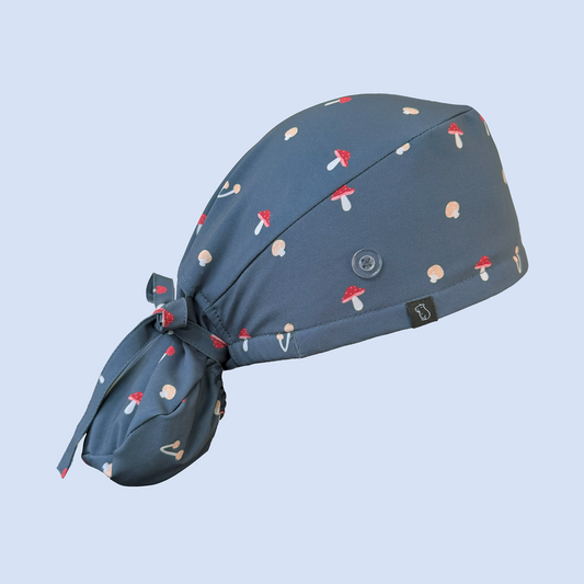 Side view of blue ponytail scrub cap decorated with a whimsical mushroom print in red, yellow, and white