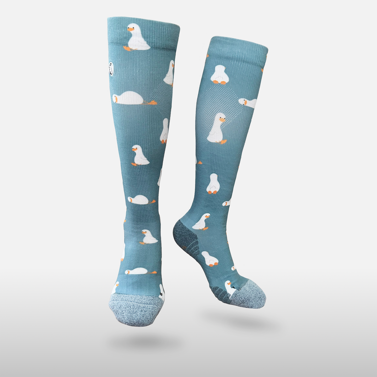 Floating blue/teal compression sock with print featuring various ducks on light grey background
